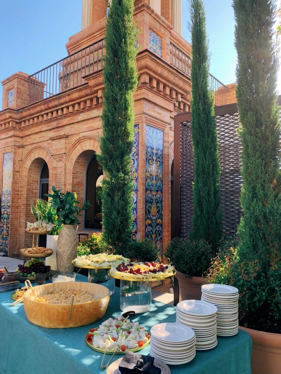 Buffet en la terraza con el edificio de ladrillo y cipreses al fondo